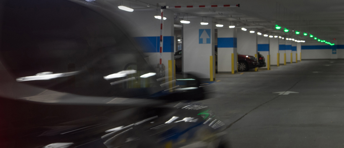 Vehicle passing under a gate into a well-lit parking garage with vacant spots and green overhead M5 smart sensors.
