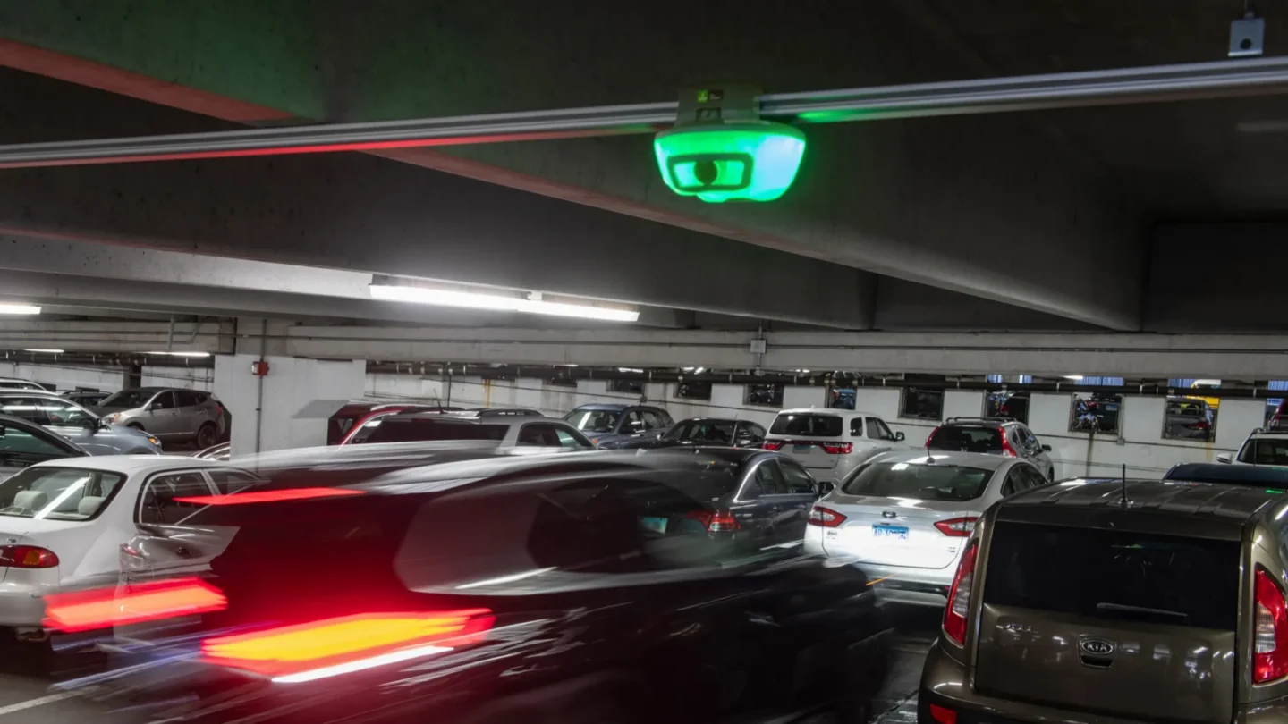Parking garage with vehicles and overhead parking guidance sensor from Park Assist indicating available space