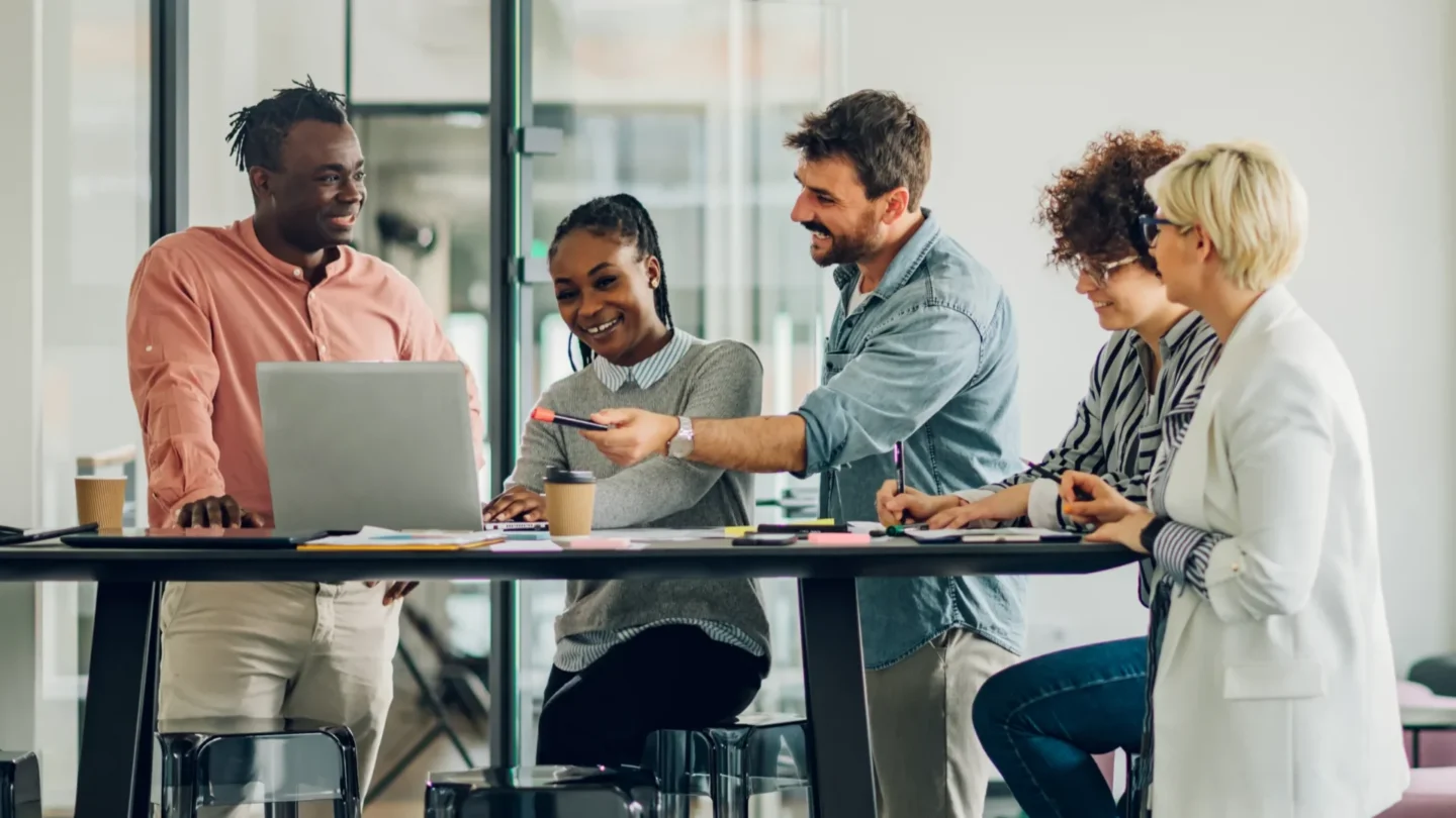 Employees collaborating around a table using laptops and mobile devices in an office with ATLAS