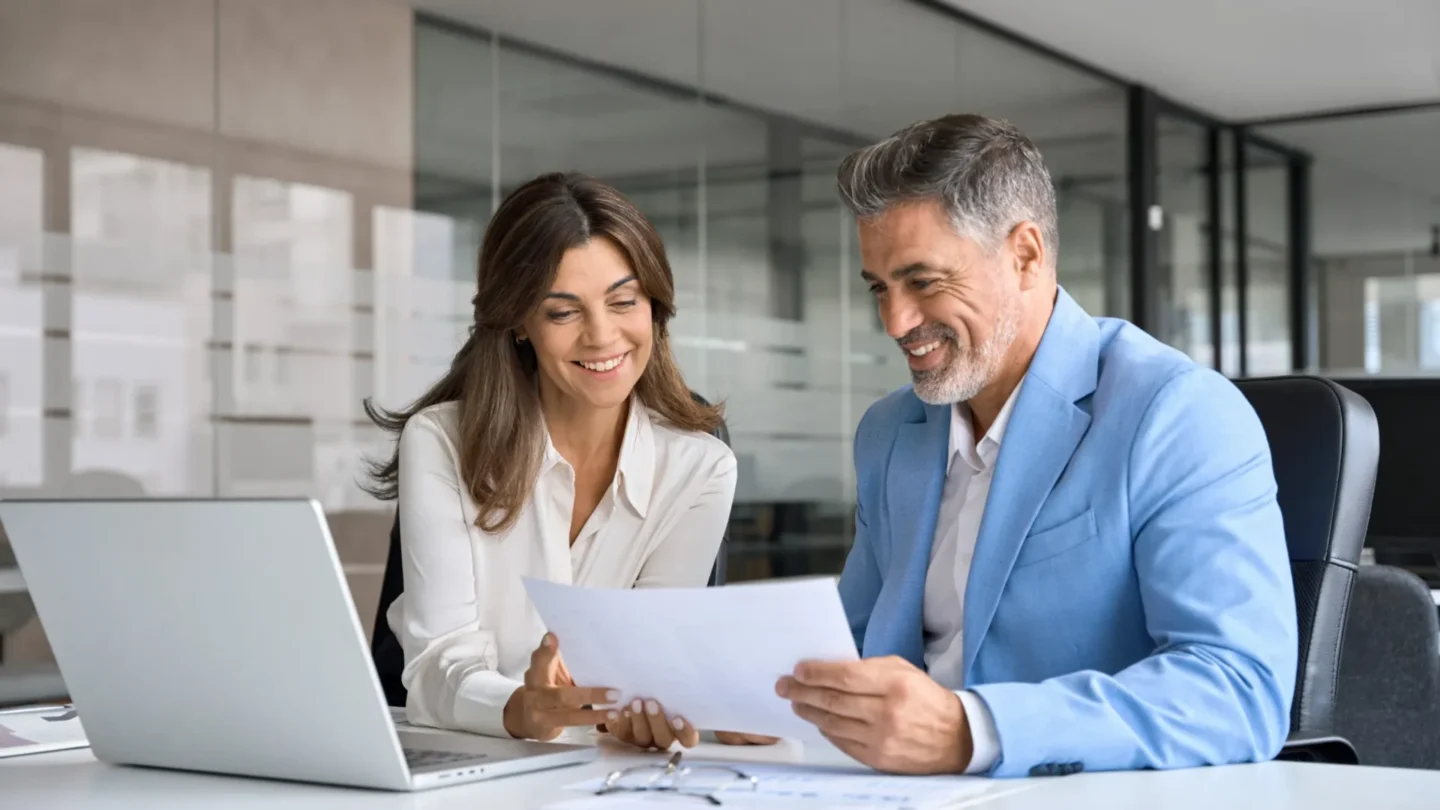 Two property managers reviewing documents together at a desk with a laptop in an office