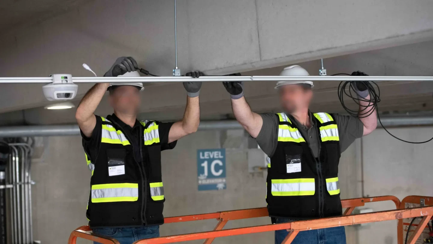 Two technicians installing M5 sensors on the ceiling of a parking garage