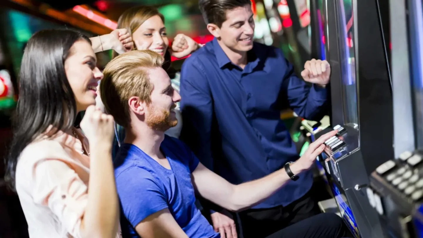 Group of people cheering as man plays slot machine in casino entertainment venue