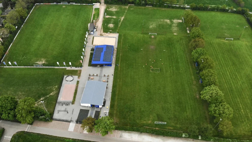 Aerial view of Angerlo Vooruit Football Club's sports fields and clubhouse, showing multiple pitches, solar panels, and training areas.